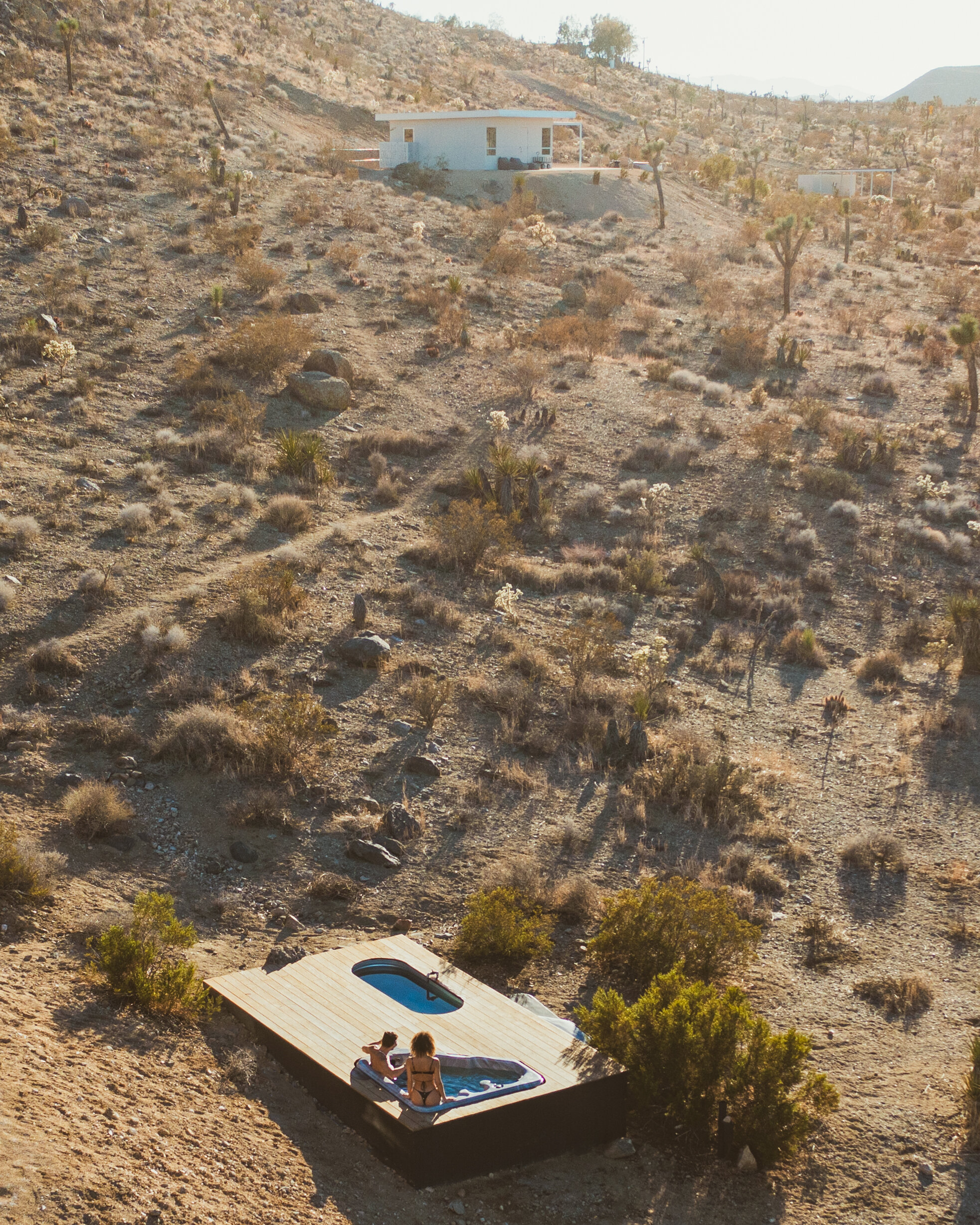 Golden-hour aerial of two guests in the hot tub at Pause House AM near Joshua Tree